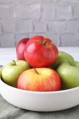 Fresh red and green apples in bowl on white table near grey textured wall, closeup