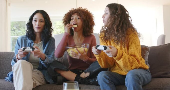Diverse friends grabbing controllers in living room, crunching chips and reacting to game start