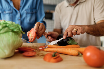 Portrait of happy senior mid aged mature couple prepering meal with fresh vegatebles in kitchen at hpme