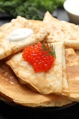 Delicious crepes with red caviar and sour cream on black table, closeup