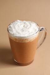 Delicious pumpkin latte with whipped cream in glass cup on beige background, closeup