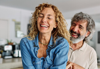 Portrait of happy senior mid aged mature couple prepering meal and having fun dancing and embracing in kitchen at hpme