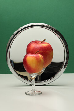 Still life with magnifying mirror and fruit. Apple and concave mirror on green background. Photo with great depth of field. 