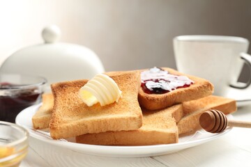 Fresh toasted bread slices served with butter, jam and tea on white wooden table, closeup