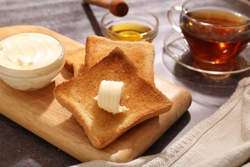 Fresh toasted bread slices with butter, honey and tea on grey table, closeup