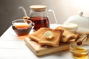 Fresh toasted bread slices served with butter, honey and tea on white wooden table