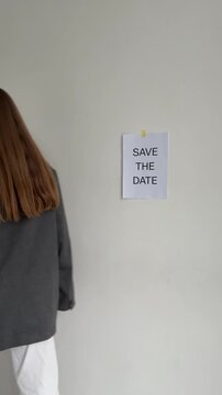 woman sticking a save the date poster on the wall