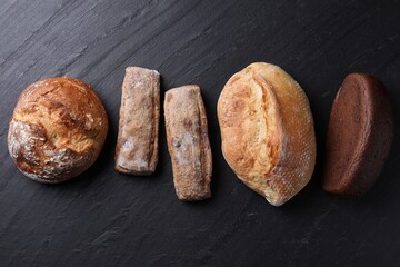 Different types of bread loaves on black table, flat lay