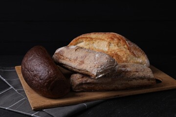 Different types of bread loaves on black table, closeup