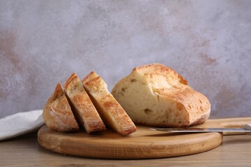 Cut fresh bread and knife on wooden table, closeup