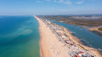 Aerial view captures Praia de Faro by Ria Formosa in Portugal. People enjoy the beach and water with boats in the water and buildings along the shore