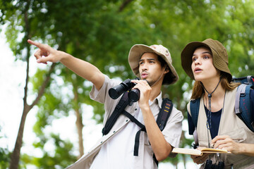 Two explorers use a notebook and binoculars while navigating through the forest.