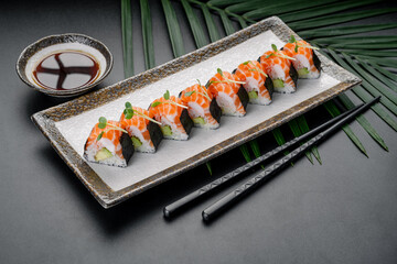 Sushi is arranged neatly on a plate next to a small bowl of sauce on a table with green leaves in the background during a dining experience