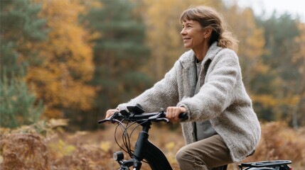 Middle-aged woman riding a bicycle in a forest during autumn. she is wearing a gray sweater and brown pants and has shoulder-length blonde hair.
