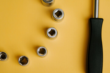 Tools arranged on a yellow background showing different sizes of sockets and a screwdriver