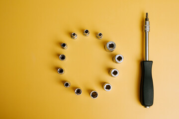 Tools arranged in a circle with a screwdriver on a yellow background in a workshop setting