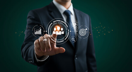 Businessman in suit pointing finger at digital interface showing team management and business growth icons, representing human resource strategy and corporate goal achievement on dark background