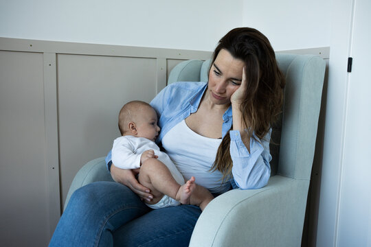 Anxious new mother holding her infant, showing signs of postpartum depression