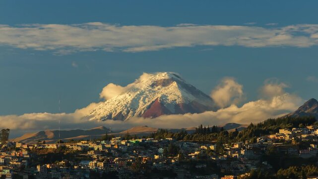 Spectacular timelapse of the imposing Cotopaxi volcano, covered in snow and surrounded by clouds, rising above the skyline of Quito, Ecuador.
