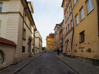 Fototapeta premium Empty, historic cobblestone street bordered by tall, traditional pastel-colored townhouses in the reconstructed Old Town of Warsaw, Poland.