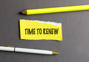 Text time to renew written on yellow paper with pencil and pen on gray background