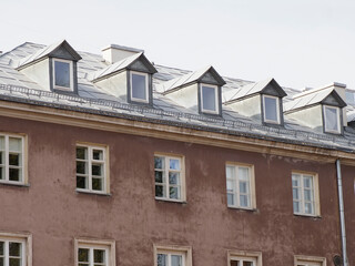Upper section of an elegant, light-brown historic facade with numerous small dormer windows and a grey tiled roof.