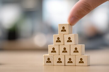 Hand places final wooden block atop a pyramid of people icons.