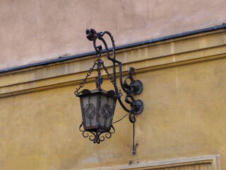 Ornate vintage black wrought-iron street lamp attached to an aged yellow wall in the historic Old...