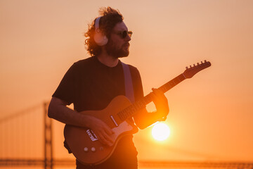 Hipster street musician in black playing electric guitar in street outdoors on sunset