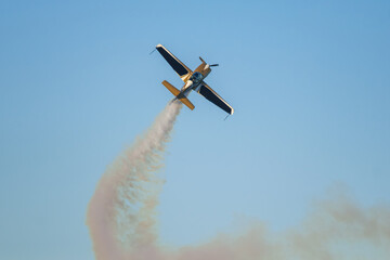 Golden stunt aerobatic plane performing stunts in blue sky with smoke trail. Concept of speed, difficulty, precision, risk