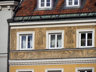 Obraz premium Close-up of a yellow historic building facade with decorative light-colored stucco elements and three rectangular windows in Warsaw Old Town.