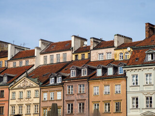 General view of the unified facades of historic townhouses with varying pastel colors and red tiled roofs in Warsaw Old Town, Poland.