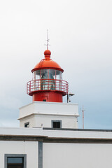 Red and white lighthouse structure with a prominent lantern, standing tall against a cloudy sky, symbolizing guidance and safety for maritime navigation