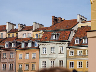 Wide shot of multiple rows of beautifully restored colorful townhouses with red roofs in Warsaw Old Town on a clear day.