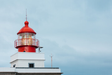 Red and white lighthouse with a glass lantern, standing tall against a cloudy sky, symbolizing guidance and safety for maritime navigation and coastal scenery