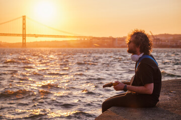 Hipster street musician in black playing electric guitar in the street on sunset