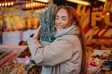 Obraz premium Woman holds small tree in market filled with decorations during festive season in winter