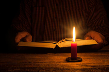 Hands hold an open book in the warm glow of a candle. This calm scene reflects the magic of reading by candlelight and offers a moment of peace in a hectic world.