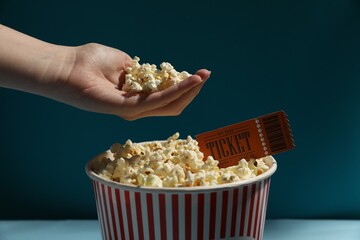 Woman taking tasty popcorn on light blue background, closeup