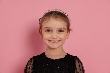 Portrait of smiling little girl in headband on pink background