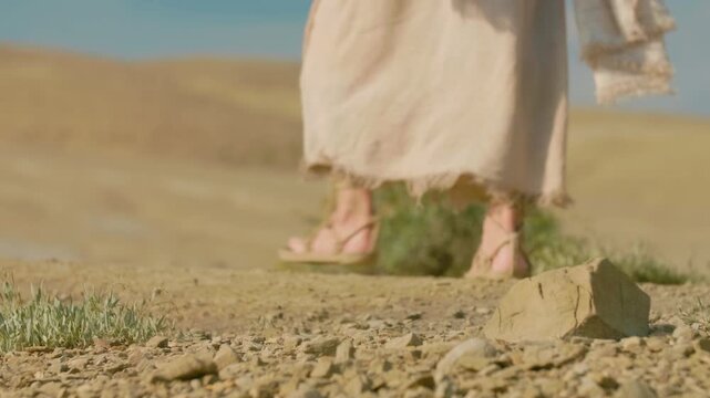 A detailed close-up showing the feet of a traveler clad in ancient rope sandals, standing beside a prominent rock on parched, cracked earth.