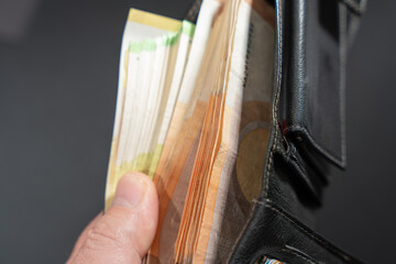 Hand holds an open black leather wallet packed with euro banknotes. Close-up view suggests cash payment, budgeting, and financial security.