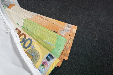 A white envelope reveals a stack of euro banknotes on a dark background. Symbol of salary, gift money, saving, or hidden cash.