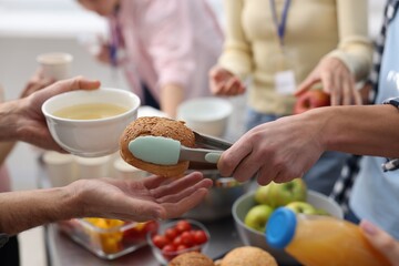 Volunteers giving food to homeless people in shelter, closeup