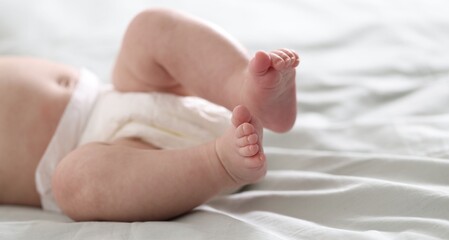 Cute newborn baby in diaper lying on bed indoors, closeup. Space for text