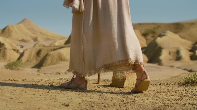 Close-up showing the feet of a traveler clad in ancient rope sandals, standing beside a prominent rock on parched, cracked earth. Christian and spiritual concept