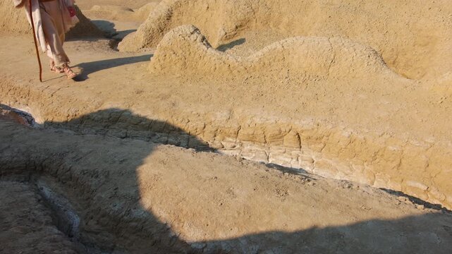 Close-up shot of a traveler's feet in ancient rope sandals, standing beside a prominent rock on parched, cracked earth. Christian and spiritual concept