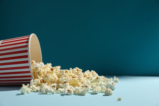 Tasty popcorn in paper cup on light blue background, closeup. Space for text
