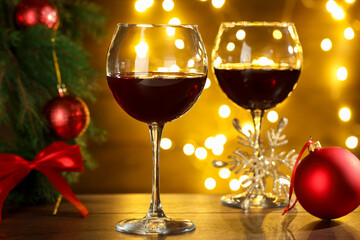 Glasses of red wine and Christmas decor on wooden table against background with blurred lights