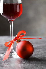 Glass of red wine and Christmas bauble on grey table, closeup